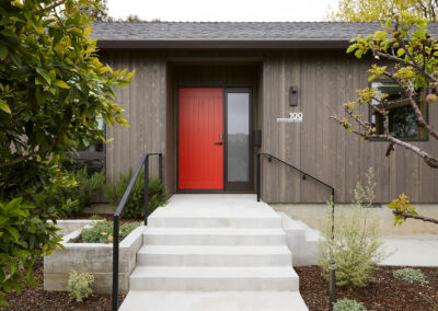 modern home exterior with gray brown wood siding and bright red door with modern lighting