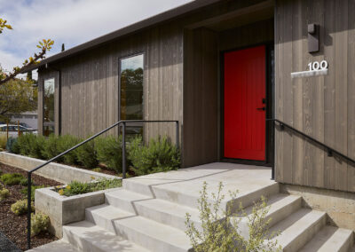 modern home exterior with gray brown wood siding and bright red door with modern lighting